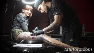 Фото тату процесса нанесения татуировки на бедро клиента. Видна рука мастера с тату-машинкой и нога клиента с начинающимся рисунком.