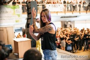 Фото тату девушки с татуировкой в стиле маори на руке, демонстрирующей свою татуировку во время выступления на сцене.