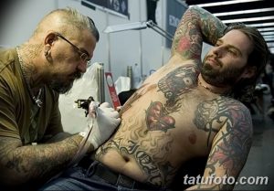 Фото процесса нанесения татуировки на грудь мужчины. Мастер тату в рабочей обстановке, клиент лежит на кушетке.