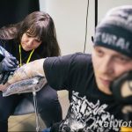 Фотография процесса нанесения татуировки на руку клиента в тату-студии: мастер в черной повязке работает над рисунком.
