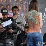 Фотография с тату-фестиваля: девушка с яркой татуировкой на спине дает интервью журналисту.