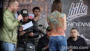 Фотография с тату-фестиваля: девушка с яркой татуировкой на спине дает интервью журналисту.