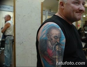 Фотография татуировки с изображением реалистичного портрета старца с длинной бородой на плече мужчины.