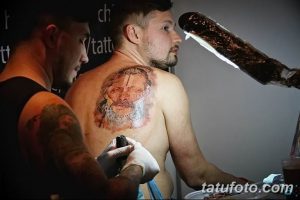 Фото процесса нанесения реалистичной портретной татуировки на спину мужчины в тату-студии.