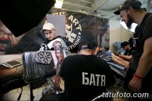 Фото тату процесса нанесения татуировки: мастер в кепке работает над рисунком на руке клиента в тату-студии.