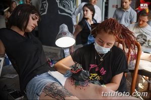 Фотография процесса татуировки, где мастер делает татуировку на ноге клиента. Видна тату-машинка, рука мастера и часть татуировки.
