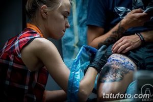 Фото тату процесса нанесения рисунка на бедро. Мастер тату делает татуировку клиентке, используя тату-машинку и черные чернила.