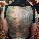 Фото тату тигра на спине мужчины. Детализированный рисунок с использованием ярких цветов и теней. Татуировка занимает всю спину.