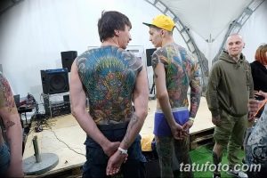 Фото тату на спине двух мужчин. Масштабные и яркие рисунки с использованием различных цветов и мотивов. Мужчины стоят спиной к спине.