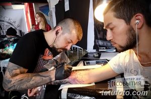 Фото тату процесса нанесения татуировки на руку клиента. Мастер в черной одежде работает над рисунком.