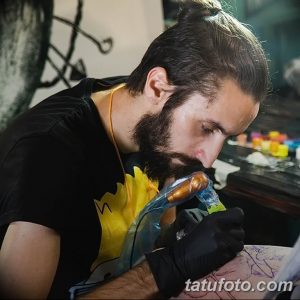 Фото тату мастера, работающего над татуировкой. Видна рука мастера с тату-машинкой и рука клиента.