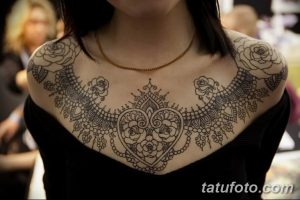 Фото тату изящного орнамента на ключицах и груди девушки. Рисунок выполнен в черном цвете и напоминает кружево.