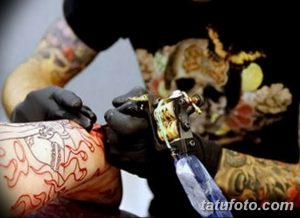 Фото процесса нанесения татуировки. Мастер в черных перчатках работает тату-машинкой над кожей клиента.