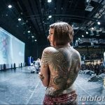 Фото тату на спине девушки на фестивале татуировок. Мастер демонстрирует работу, на заднем плане сцена и зрители.