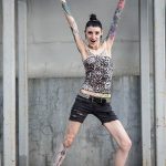 Фотография демонстрирует девушку с татуировками на руках и ногах, позирующую в дерзком и уверенном образе.