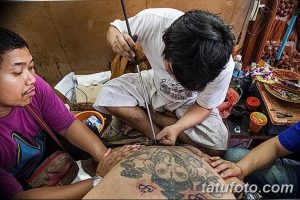 Фотография показывает мастера тату, работающего над сложным рисунком сак янт на спине клиента.