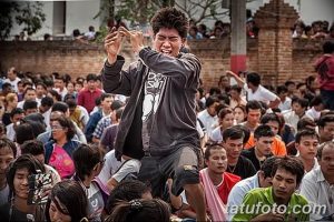 Фотография показывает традиционный тайский ритуал татуировки, где мужчина в экстазе, окруженный толпой людей, наблюдающих за процессом.