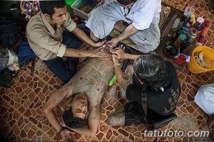 Фото тату: несколько человек участвуют в традиционном таиландском ритуале татуировки. Виден процесс нанесения рисунка и инструменты.