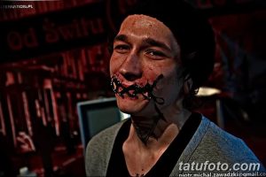 Фотография мужчины с экстремальной модификацией тела, включая татуировки и пирсинг. Видна татуировка в виде шипов вокруг рта.
