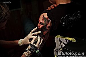 Фотография процесса нанесения реалистичной татуировки на плечо. Видна рука мастера с тату-машинкой и контуры портрета.
