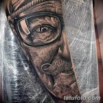 Фото тату: Черно-белая реалистичная татуировка на руке с изображением портрета старика в шапке и очках. Детализированный и выразительный рисунок.