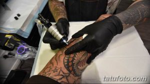 Фото процесса татуировки: мастер в черных перчатках наносит рисунок на кожу клиента с помощью тату-машинки. Детализированное изображение рабочего места.