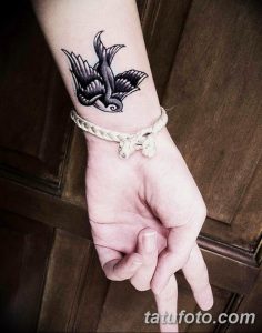 Фото тату ласточки в стиле олд скул на запястье. Черно-белый рисунок татуировки с четкими контурами и традиционными элементами.