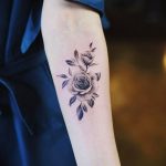 Фото тату: минималистичная татуировка розы, выполненная в технике blackwork, на предплечье. Нежный и элегантный эскиз татуировки для женщин.