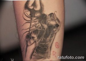 Фото татуировки Шивы на руке в черно-серых тонах. Детализированное изображение индуистского бога с трезубцем и змеями, символизирующее разрушение и созидание.