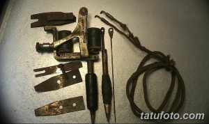 Фото старого тату-аппарата, разобранного на детали. Видны металлические пластины, пружины, катушки и провод.