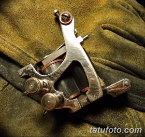 Фотография старинной тату машинки, лежащей на фоне зеленой ткани. Изображение создает атмосферу старой тату-студии и мастерства.