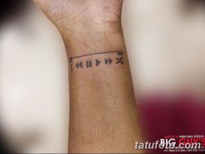 Фото тату на запястье с изображением плеера, временной шкалы и надписью. Черно-серый рисунок татуировки в минималистичном стиле.