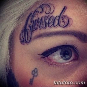 Фото тату надписи 'Cursed' на лбу девушки. Изображение демонстрирует смелый и провокационный выбор.