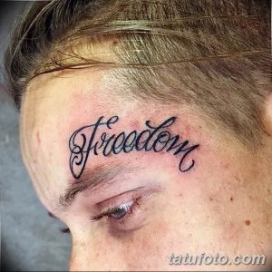 Фото татуировки на лице мужчины с надписью 'Freedom', выполненной изящным каллиграфическим шрифтом. Элегантный и минималистичный рисунок.