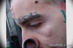 Фото татуировки с изображением усов над бровью и небольших цветов на виске. Оригинальный и экстравагантный рисунок.
