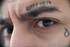 Фото тату над бровью с надписью 'CREEPER' и маленькой капелькой крови. Черно-белый рисунок татуировки на мужском лице.