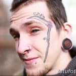 Фото тату косы на лице мужчины. Татуировка выполнена черными чернилами, расположена на щеке и спускается к подбородку.