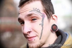 Фото тату косы на лице мужчины. Татуировка выполнена черными чернилами, расположена на щеке и спускается к подбородку.