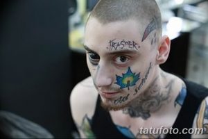 Фото тату на лице мужчины: надписи, рисунки и символы. Татуировки выполнены в различных цветах, расположены на лбу, щеках и под глазом.