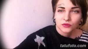 Фото тату надписи на лбу девушки с пирсингом. Татуировка выполнена черными чернилами, шрифт стилизованный, расположен над бровью.