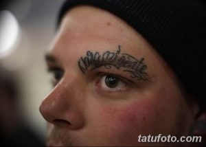 Фото мужчины с татуировкой на лбу. Над бровью видна надпись, выполненная черным цветом.