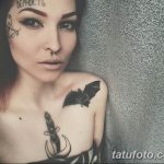 Фото девушки с татуировками на лице, шее и груди. На лбу видна надпись 'ВЕРНОСТЬ', на плече – изображение летучей мыши.