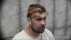 Фото тату на лбу с надписью 'Asshole' черным цветом. Крупный план лица мужчины с татуировкой, выражающей протест.