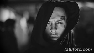 Фото тату на лице мужчины в черно-белом стиле. Надбровные дуги и щеки украшены мелкими надписями и символами, демонстрируя смелый и дерзкий выбор.