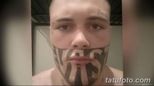 Фото татуировки на лице мужчины: крупная надпись «VAS» расположена на щеках и подбородке. Тату выполнено в черном цвете.