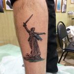 Фото тату Богини Победы с мечом и футбольным мячом на руке. Рисунок татуировки в стиле реализм, выполненный в серых тонах. Подходит для фанатов футбола и тех, кто ценит победу.