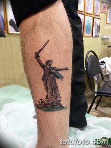 Фото тату Богини Победы с мечом и футбольным мячом на руке. Рисунок татуировки в стиле реализм, выполненный в серых тонах. Подходит для фанатов футбола и тех, кто ценит победу.