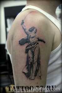Фото тату Богини Победы с мечом на плече. Рисунок татуировки в стиле реализм, выполненный в серых тонах. Подходит для тех, кто ценит силу и красоту.