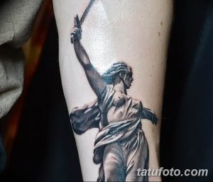 Фото тату Родина-мать на руке, выполненное в черно-серых тонах. Детализированный рисунок татуировки с акцентом на светотень.