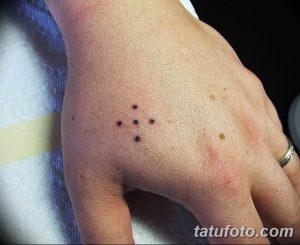 Фотография минималистичной татуировки созвездия из точек на тыльной стороне руки. Татуировка выполнена черными чернилами и выглядит очень изящно.